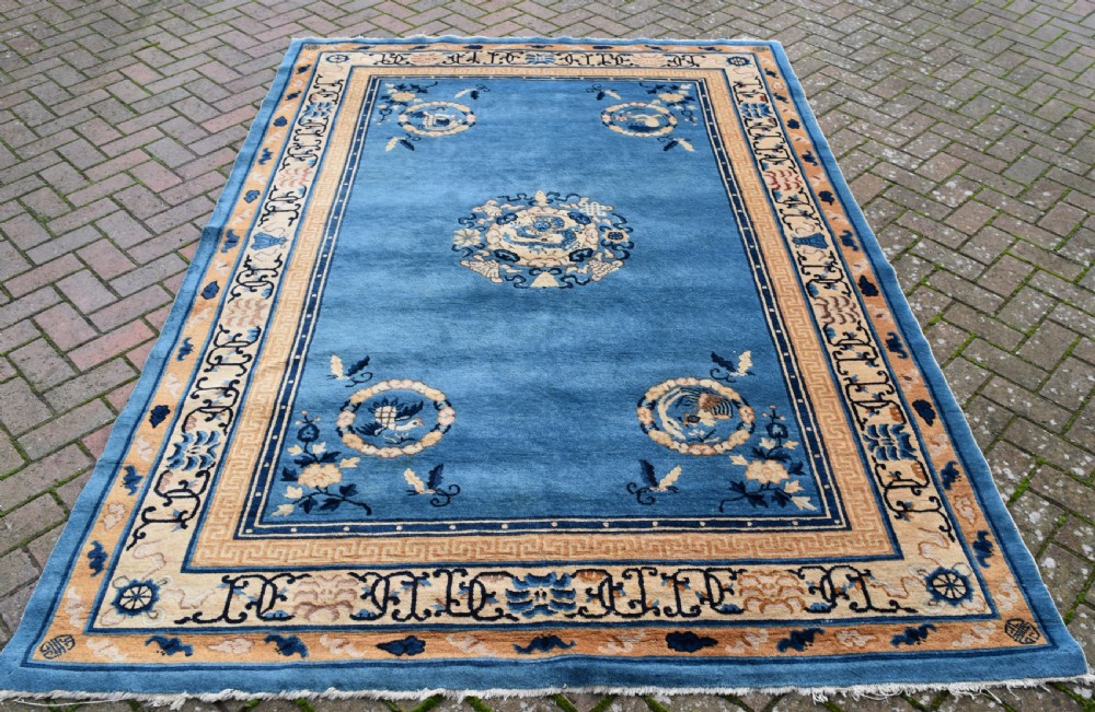 A rectangular hand-knotted wool carpet featuring a bright blue central field decorated with circular floral medallions and a broad beige geometric border.