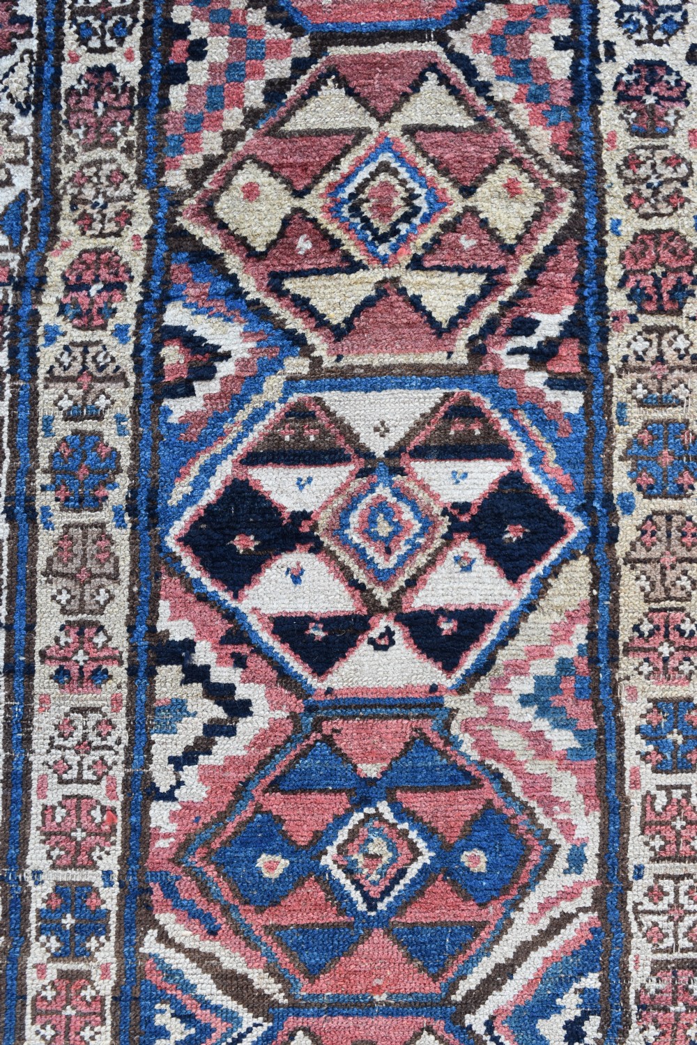 An exceptionally long, narrow hand-knotted wool runner rug featuring a series of geometric diamond medallions in red, navy blue, and cream along a decorated field with multi-banded patterned borders. View III