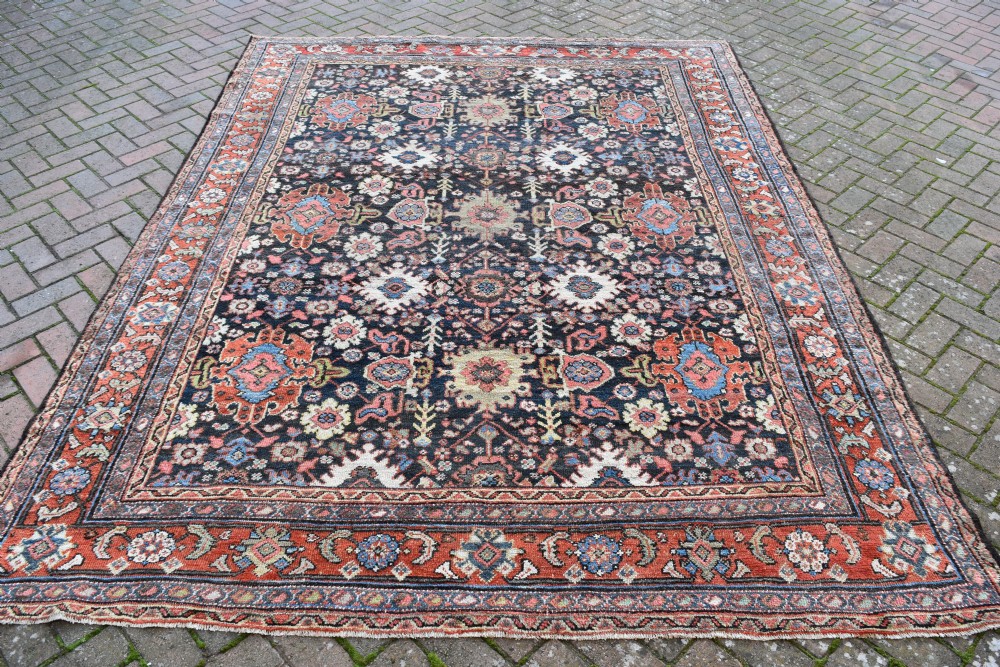 A large rectangular hand-knotted wool carpet featuring a dark navy central field filled with geometric floral motifs and framed by a wide terracotta border.