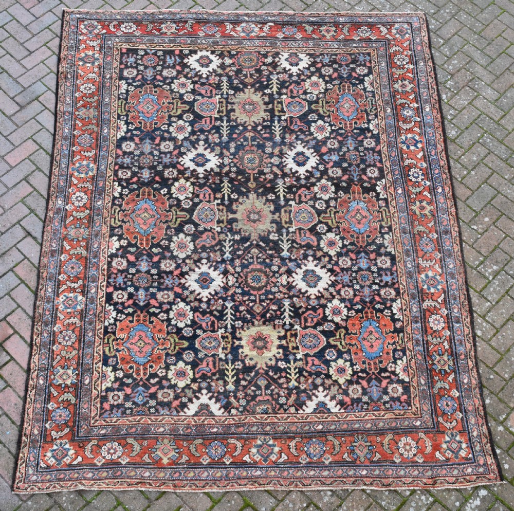 A large rectangular hand-knotted wool carpet featuring a dark navy central field filled with geometric floral motifs and framed by a wide terracotta border. View VIII