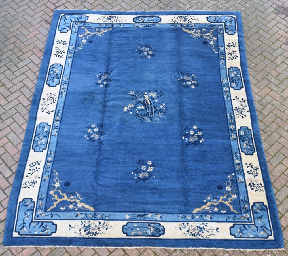 An antique blue and cream Chinese Peking carpet featuring floral motifs and a central bird design within decorative borders.