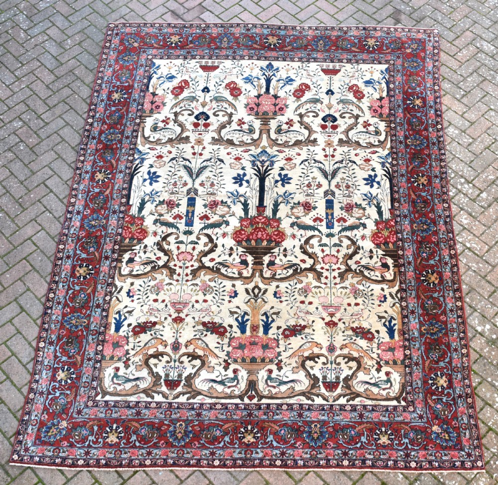 A large hand-knotted Persian Qum carpet featuring an ivory central field patterned with birds, urns, and floral motifs within a dark red border.