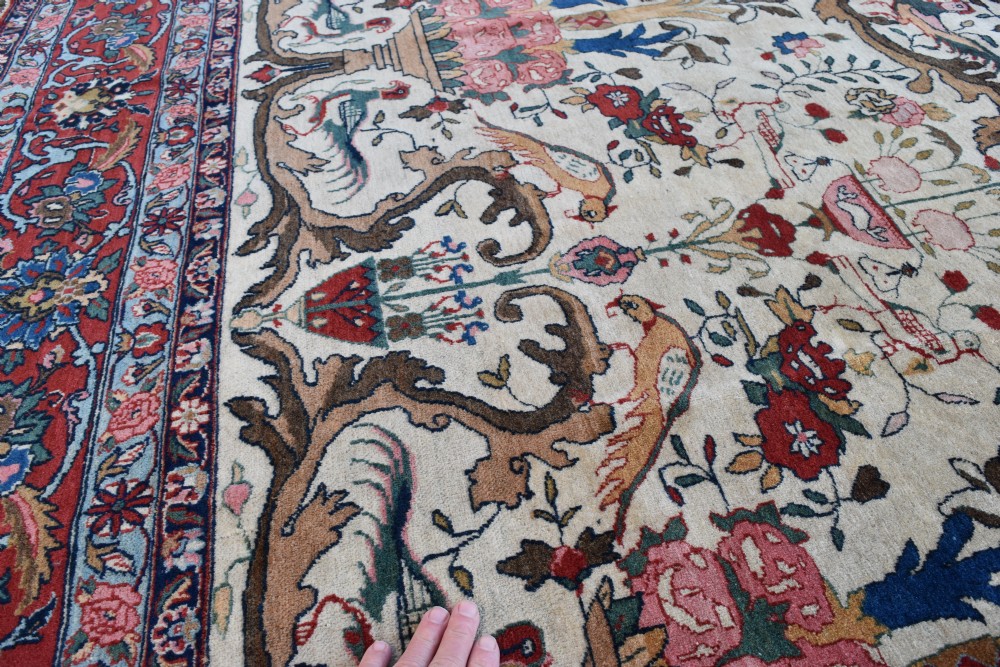 A large hand-knotted Persian Qum carpet featuring an ivory central field patterned with birds, urns, and floral motifs within a dark red border. View V