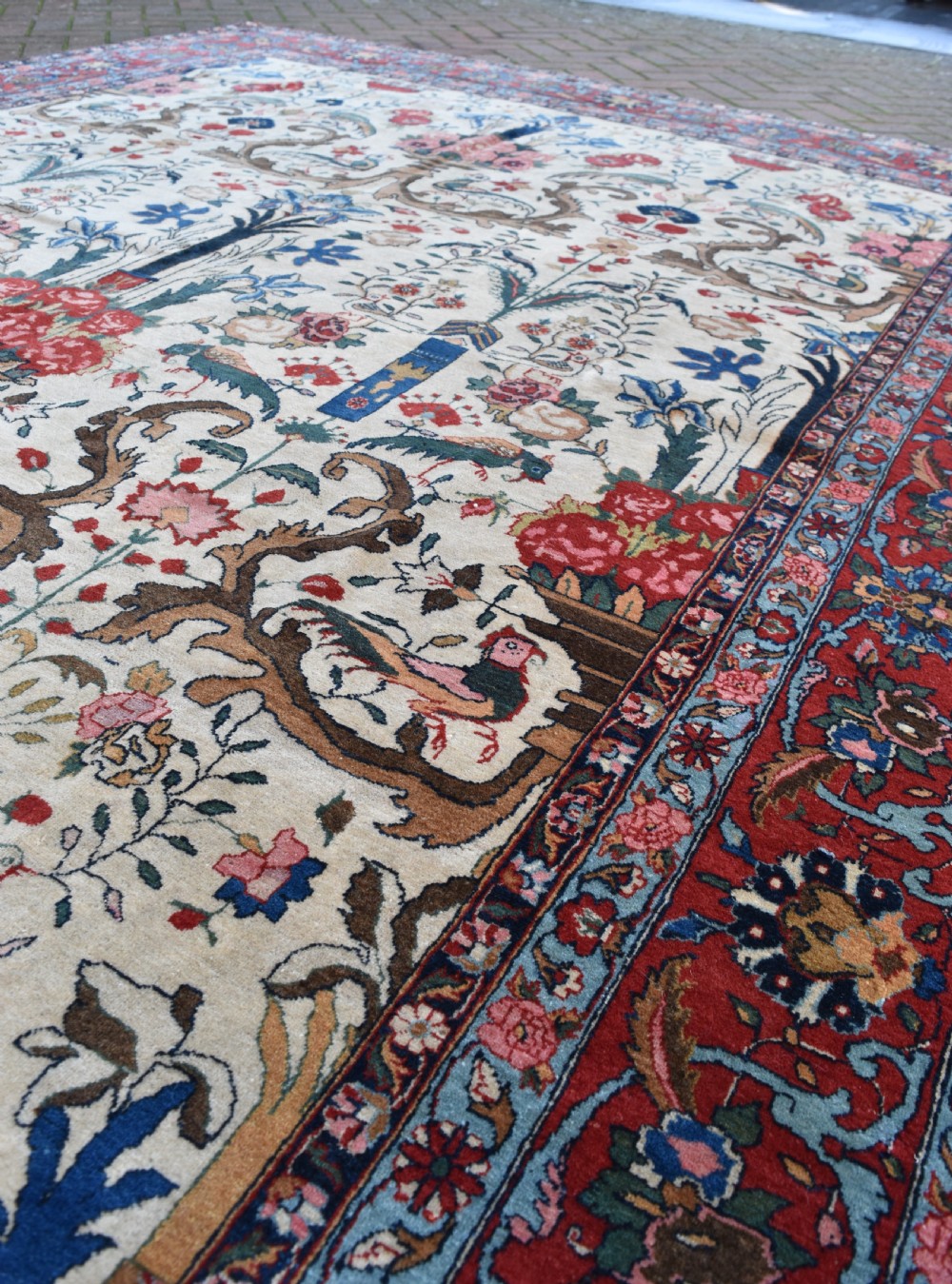 A large hand-knotted Persian Qum carpet featuring an ivory central field patterned with birds, urns, and floral motifs within a dark red border. View VI