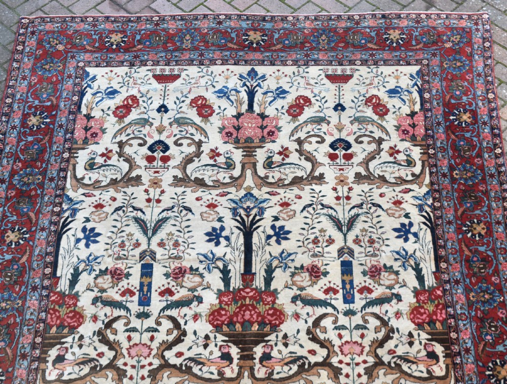 A large hand-knotted Persian Qum carpet featuring an ivory central field patterned with birds, urns, and floral motifs within a dark red border. View X