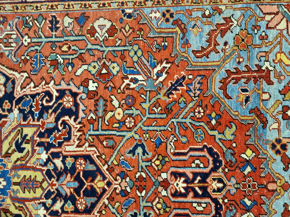 An antique hand-knotted Persian Heriz carpet with a central geometric navy medallion on a terracotta red field with light blue spandrels. View II