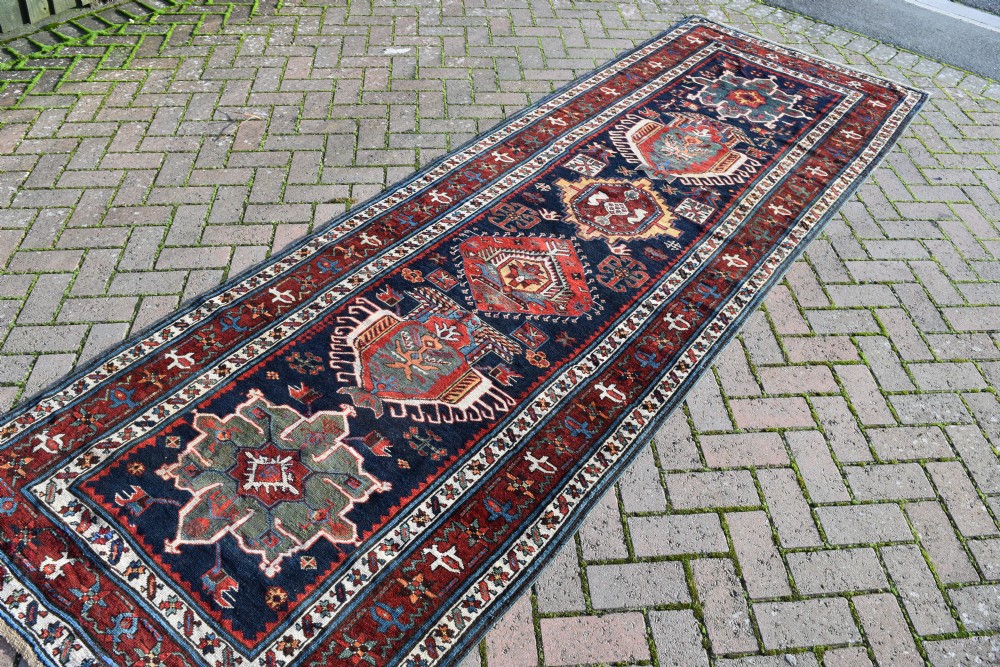 An antique Karadagh hand-knotted wool runner rug featuring geometric medallions on a navy blue central field framed by a wide terracotta red patterned border. View III