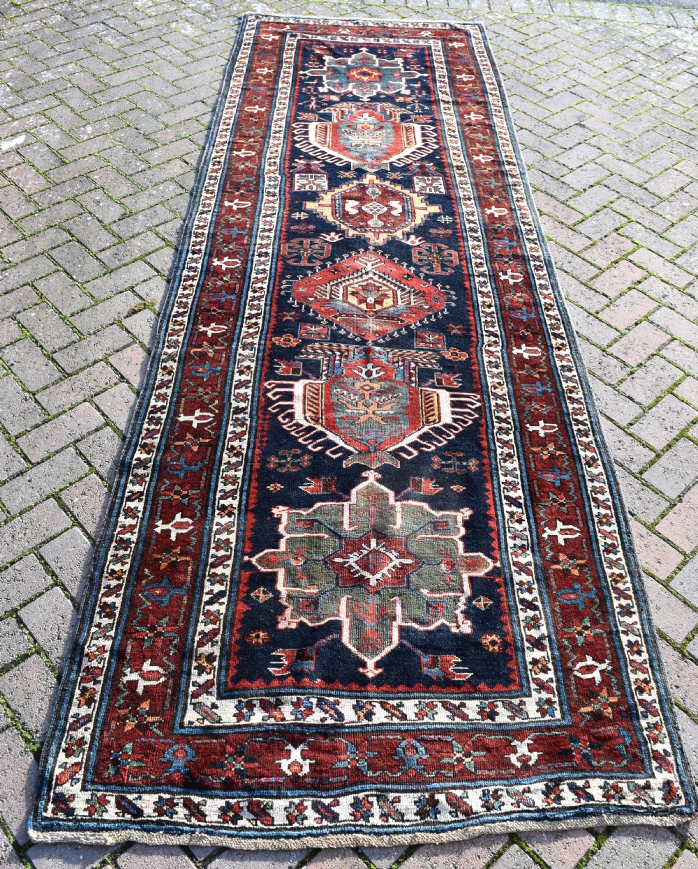 An antique Karadagh hand-knotted wool runner rug featuring geometric medallions on a navy blue central field framed by a wide terracotta red patterned border. View IX