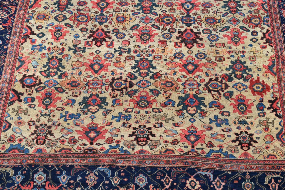 A large square hand-knotted antique Ferahan wool carpet featuring an all-over repeating geometric and floral pattern on a cream field, framed by a wide navy blue border. View III