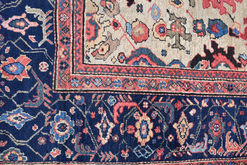 A large square hand-knotted antique Ferahan wool carpet featuring an all-over repeating geometric and floral pattern on a cream field, framed by a wide navy blue border. View VII
