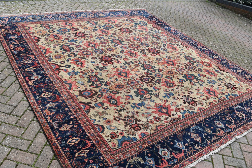 A large square hand-knotted antique Ferahan wool carpet featuring an all-over repeating geometric and floral pattern on a cream field, framed by a wide navy blue border. View VIII