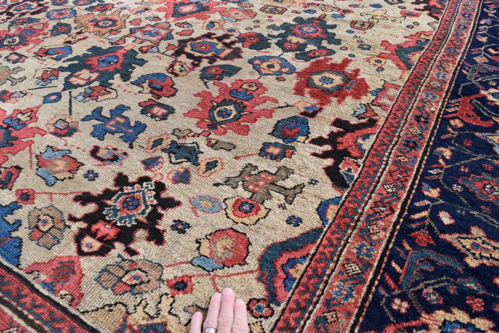 A large square hand-knotted antique Ferahan wool carpet featuring an all-over repeating geometric and floral pattern on a cream field, framed by a wide navy blue border. View IX
