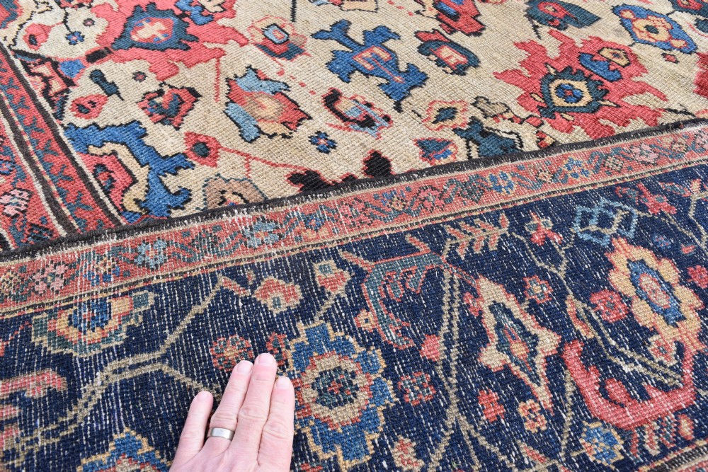 A large square hand-knotted antique Ferahan wool carpet featuring an all-over repeating geometric and floral pattern on a cream field, framed by a wide navy blue border. View X