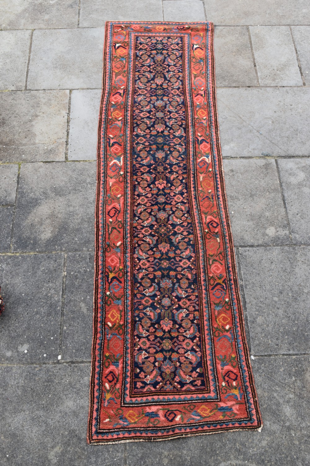 A long narrow hand-knotted antique Kurdish wool rug runner featuring a dark navy central field with repeating floral lattice patterns framed by a terracotta border.