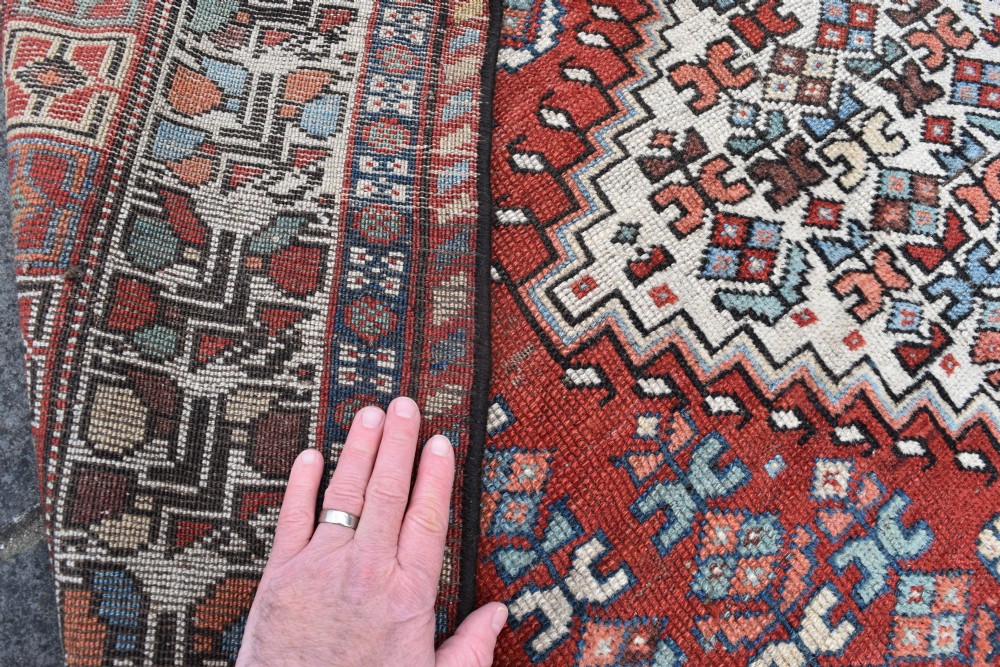 An antique hand-knotted Luri wool carpet showcasing a terracotta red field with central cream diamond medallions and geometric tribal borders. View V