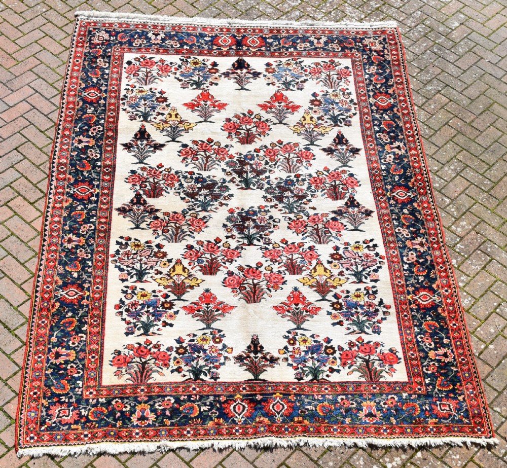 A large hand-knotted Bakhtiari carpet featuring an ivory field filled with repeating floral shrub motifs framed by a wide navy blue and red ornate border.