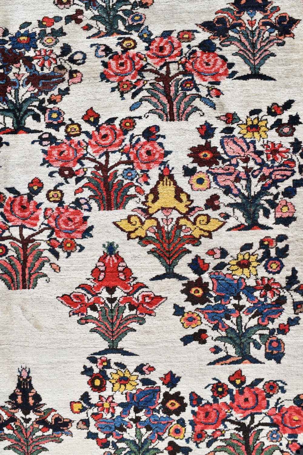 A large hand-knotted Bakhtiari carpet featuring an ivory field filled with repeating floral shrub motifs framed by a wide navy blue and red ornate border. View II