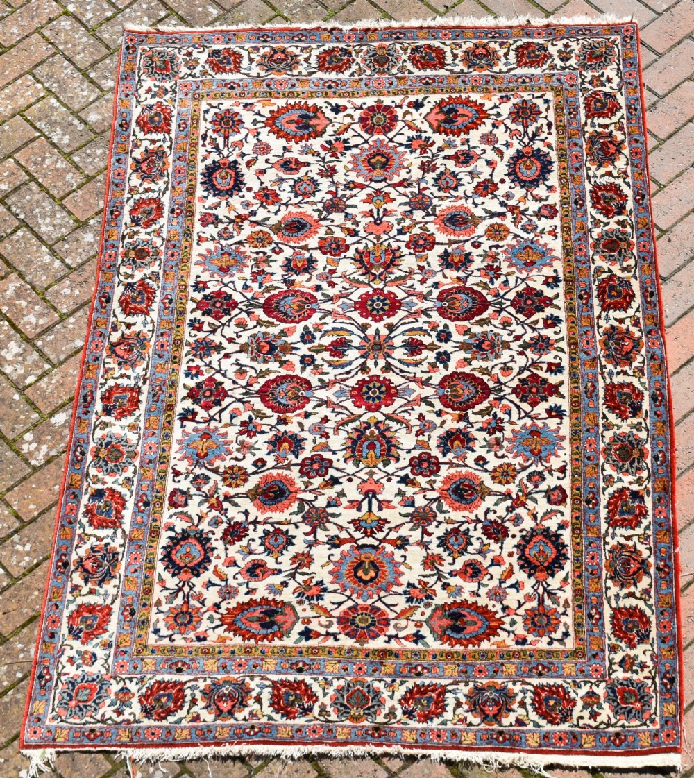 An antique hand-knotted Persian Qum rug featuring an ivory field filled with red and blue floral motifs, surrounded by a multi-band decorative border.