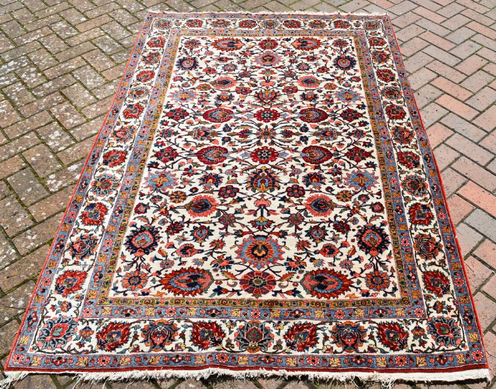 An antique hand-knotted Persian Qum rug featuring an ivory field filled with red and blue floral motifs, surrounded by a multi-band decorative border. View II
