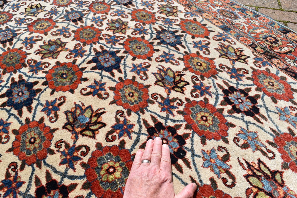 An antique hand-knotted Persian Veramin rug displaying a repeated Mina Khani floral pattern on a cream field framed by multiple dark red and blue decorative borders. View IV