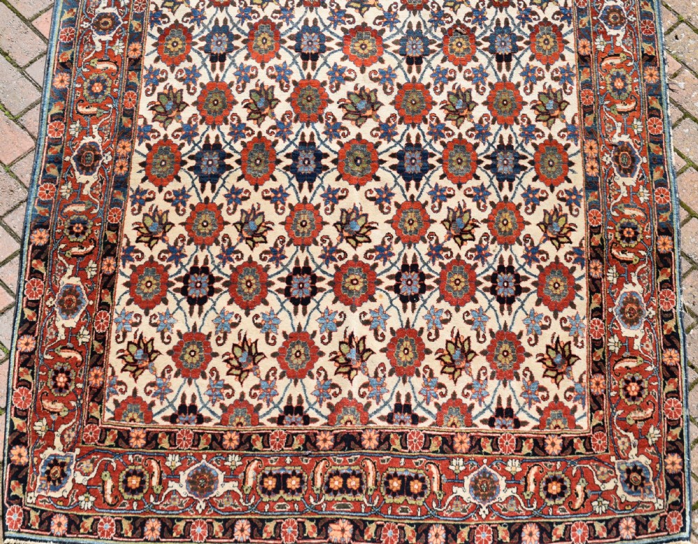 An antique hand-knotted Persian Veramin rug displaying a repeated Mina Khani floral pattern on a cream field framed by multiple dark red and blue decorative borders. View VII