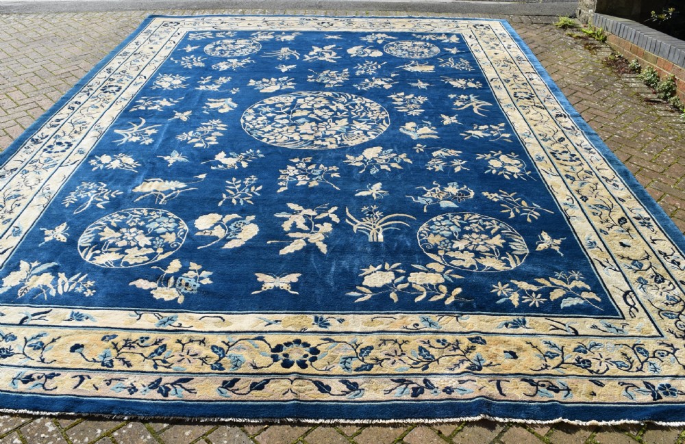 A large indigo blue wool carpet with a central floral medallion, smaller roundels, butterfly details, and a cream floral border.
