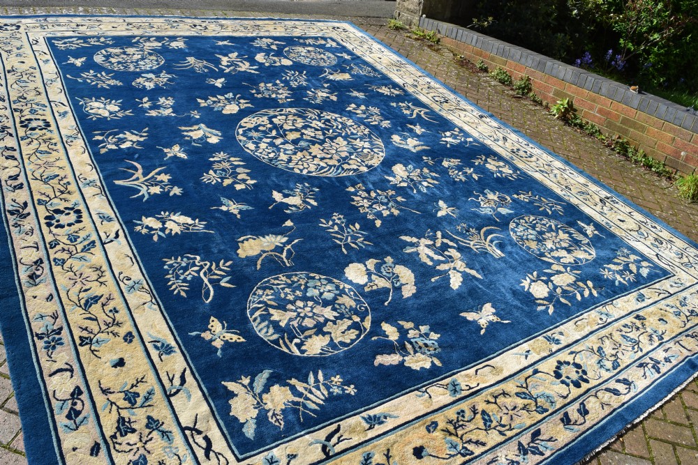 A large indigo blue wool carpet with a central floral medallion, smaller roundels, butterfly details, and a cream floral border. View II