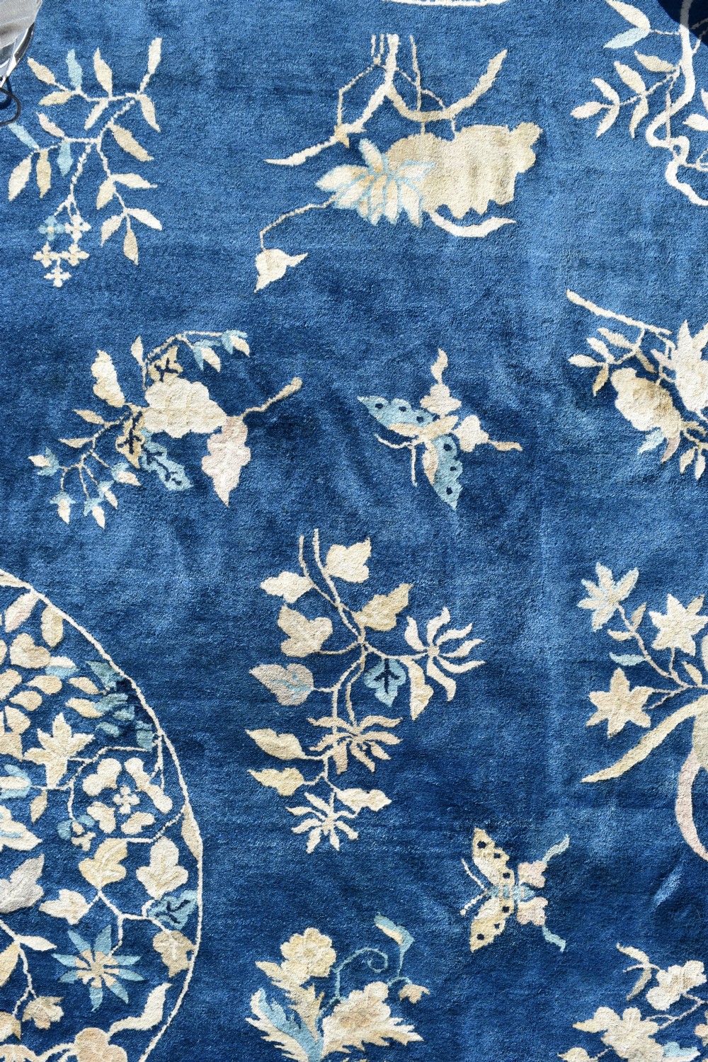 A large indigo blue wool carpet with a central floral medallion, smaller roundels, butterfly details, and a cream floral border. View III