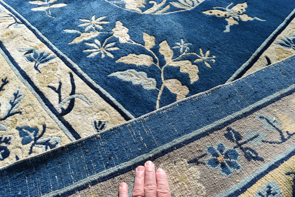 A large indigo blue wool carpet with a central floral medallion, smaller roundels, butterfly details, and a cream floral border. View IV