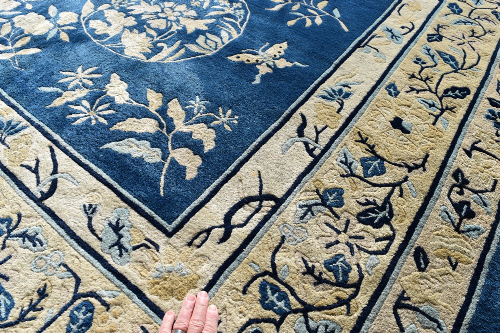 A large indigo blue wool carpet with a central floral medallion, smaller roundels, butterfly details, and a cream floral border. View V