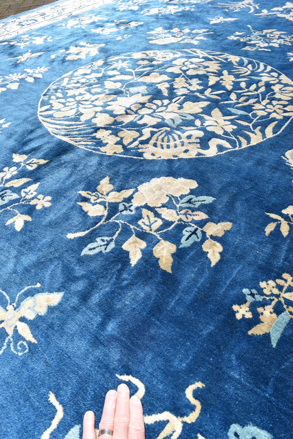 A large indigo blue wool carpet with a central floral medallion, smaller roundels, butterfly details, and a cream floral border. View VI