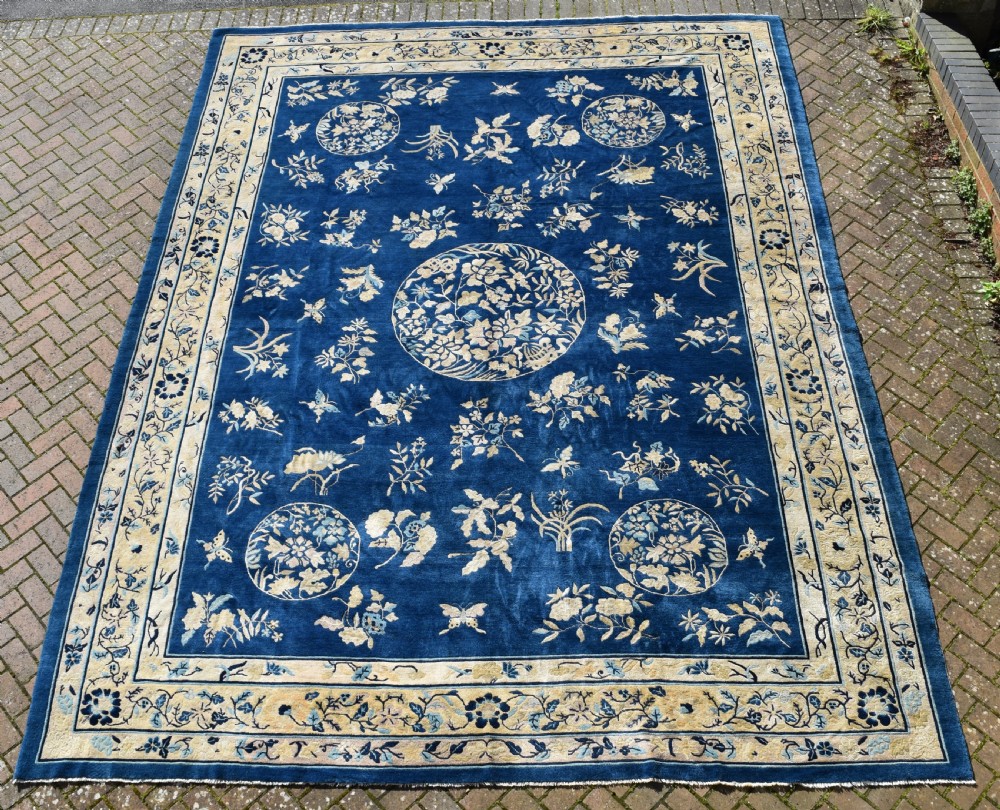 A large indigo blue wool carpet with a central floral medallion, smaller roundels, butterfly details, and a cream floral border. View VII