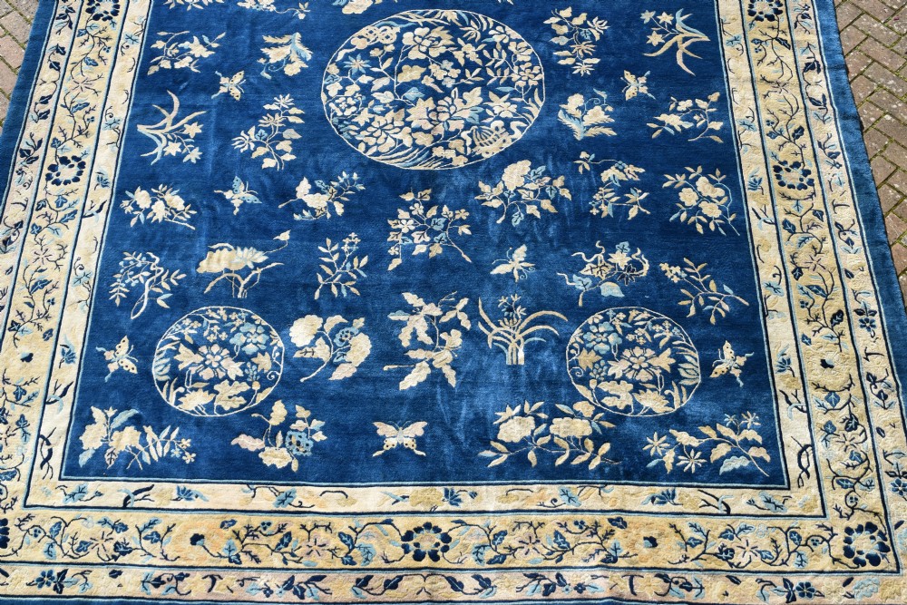 A large indigo blue wool carpet with a central floral medallion, smaller roundels, butterfly details, and a cream floral border. View IX