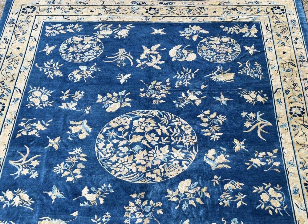 A large indigo blue wool carpet with a central floral medallion, smaller roundels, butterfly details, and a cream floral border. View X