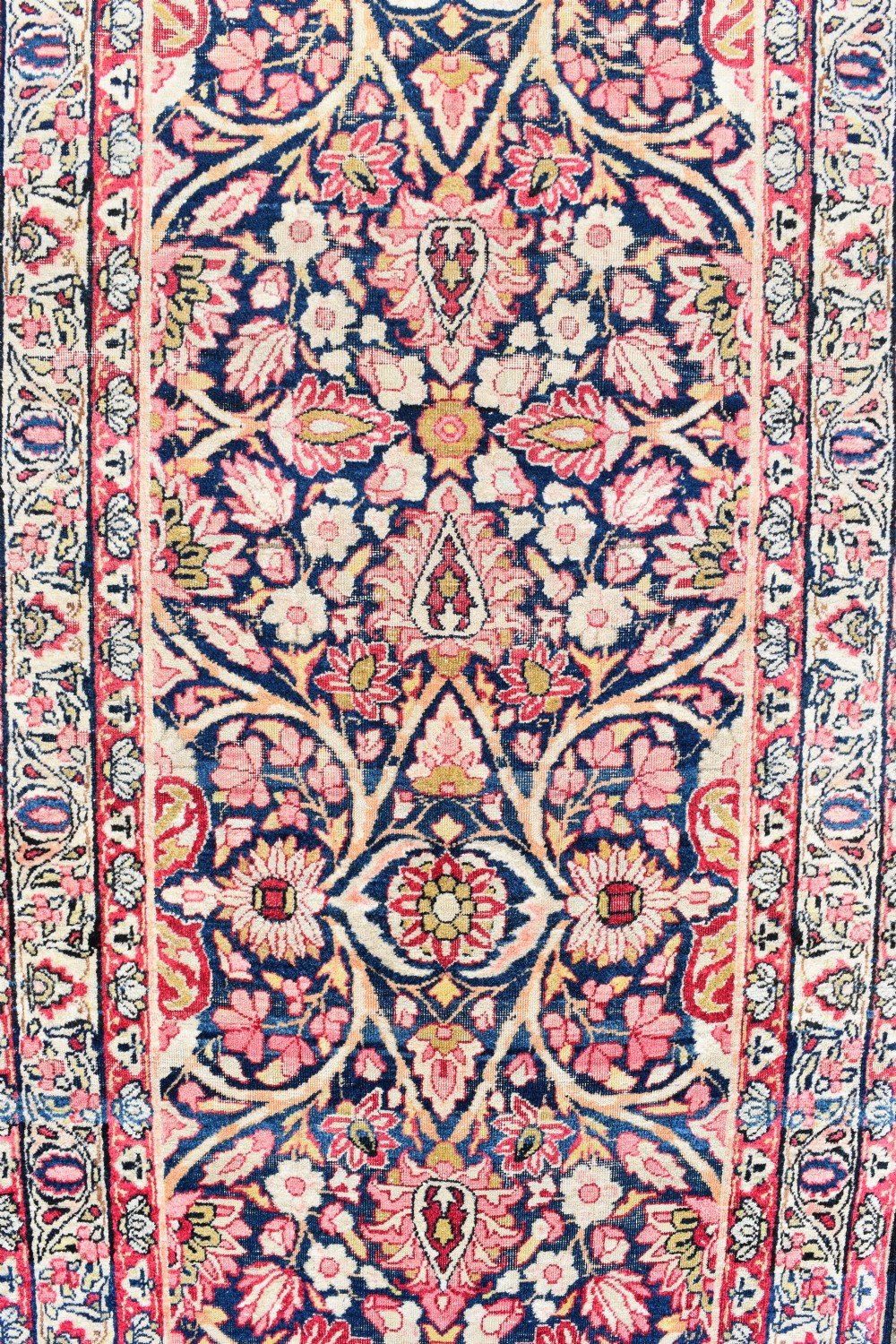 An exceptionally long and narrow hand-knotted antique Kirman rug runner featuring detailed floral medallion motifs in pink, navy blue, and cream. View III