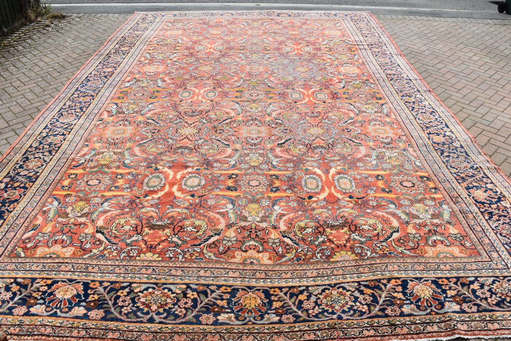 An oversized antique Persian Mahal wool carpet with a floral arabesque pattern on a terracotta field and a dark navy border.
