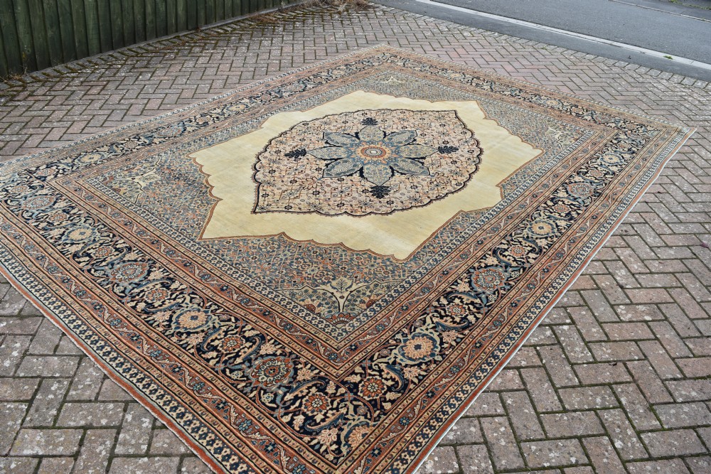 A large hand-knotted antique Persian Hajji Jalili carpet featuring a central star-shaped medallion on a cream field surrounded by dark blue floral borders. View IV
