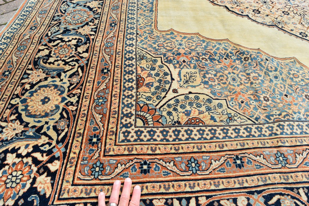 A large hand-knotted antique Persian Hajji Jalili carpet featuring a central star-shaped medallion on a cream field surrounded by dark blue floral borders. View VI