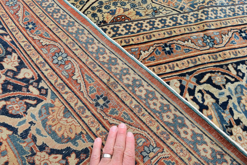 A large hand-knotted antique Persian Hajji Jalili carpet featuring a central star-shaped medallion on a cream field surrounded by dark blue floral borders. View VII
