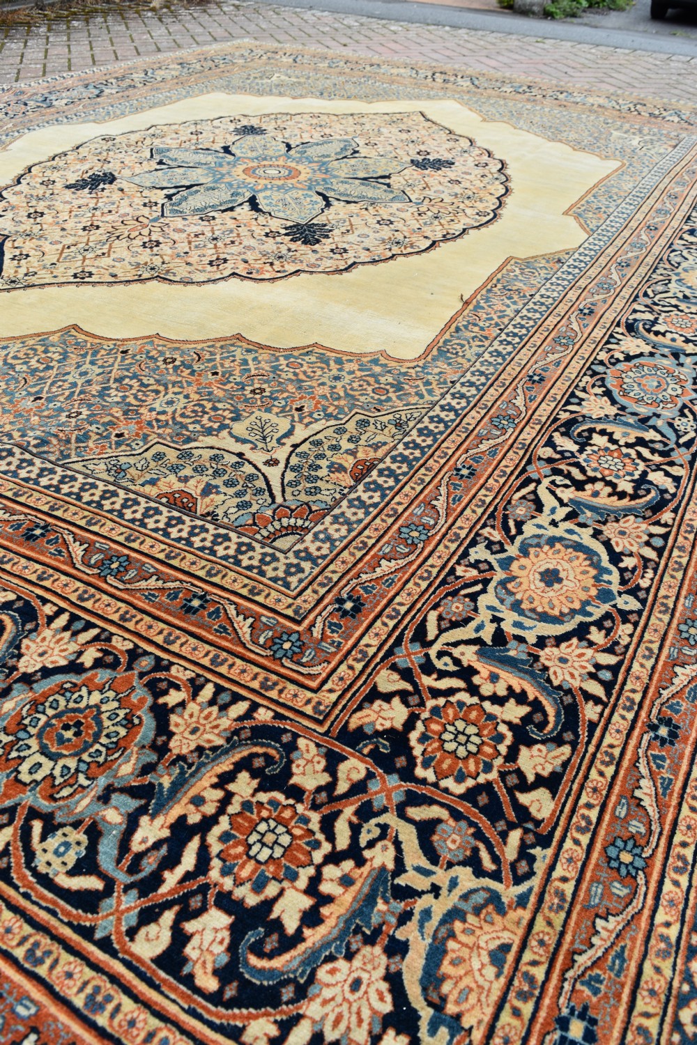 A large hand-knotted antique Persian Hajji Jalili carpet featuring a central star-shaped medallion on a cream field surrounded by dark blue floral borders. View X