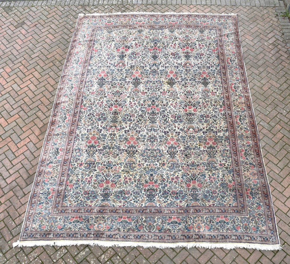 A large hand-knotted Persian Kirman room-size carpet featuring an intricate floral and vase pattern in cream, rose pink, and slate blue.