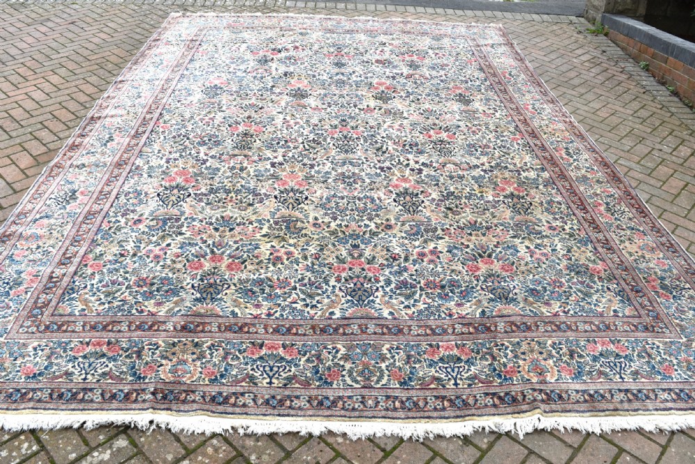 A large hand-knotted Persian Kirman room-size carpet featuring an intricate floral and vase pattern in cream, rose pink, and slate blue. View X