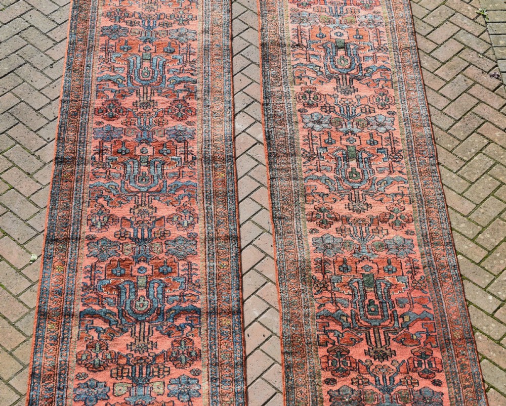 A pair of exceptionally long, narrow antique Persian Hamadan runners featuring intricate geometric and stylized floral motifs in blue and ivory on a terracotta wool ground. View IV
