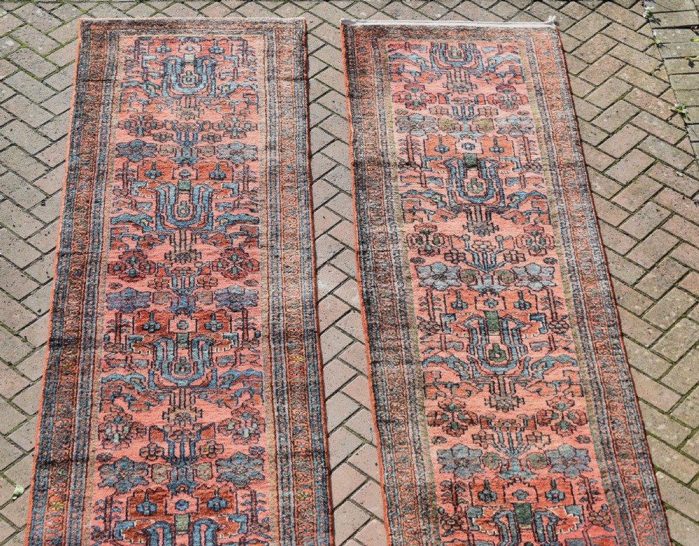 A pair of exceptionally long, narrow antique Persian Hamadan runners featuring intricate geometric and stylized floral motifs in blue and ivory on a terracotta wool ground. View V