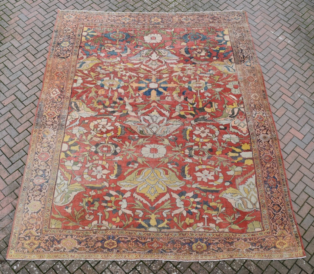 A large antique Persian Sultanabad hand-knotted wool carpet with large botanical palmettes on a terracotta field enclosed by multi-band borders.