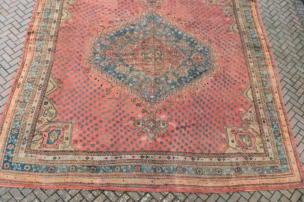 A large square hand-knotted wool Ushak carpet featuring a coral red field, a central teal medallion, cream corner spandrels, and patterned borders. View II