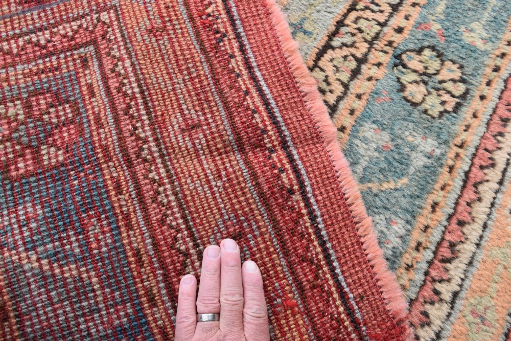 A large square hand-knotted wool Ushak carpet featuring a coral red field, a central teal medallion, cream corner spandrels, and patterned borders. View X