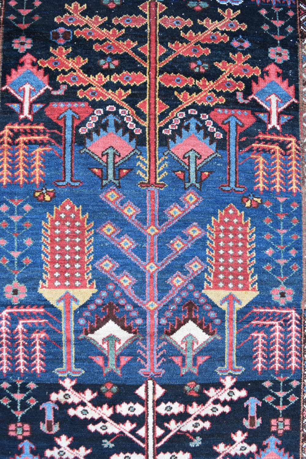 A long antique Persian Bakhtiari runner rug featuring stylised tree motifs in red, blue, and pink on a dark navy ground with a geometric border. View II