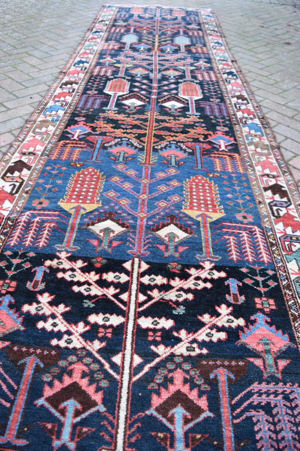 A long antique Persian Bakhtiari runner rug featuring stylised tree motifs in red, blue, and pink on a dark navy ground with a geometric border. View IV