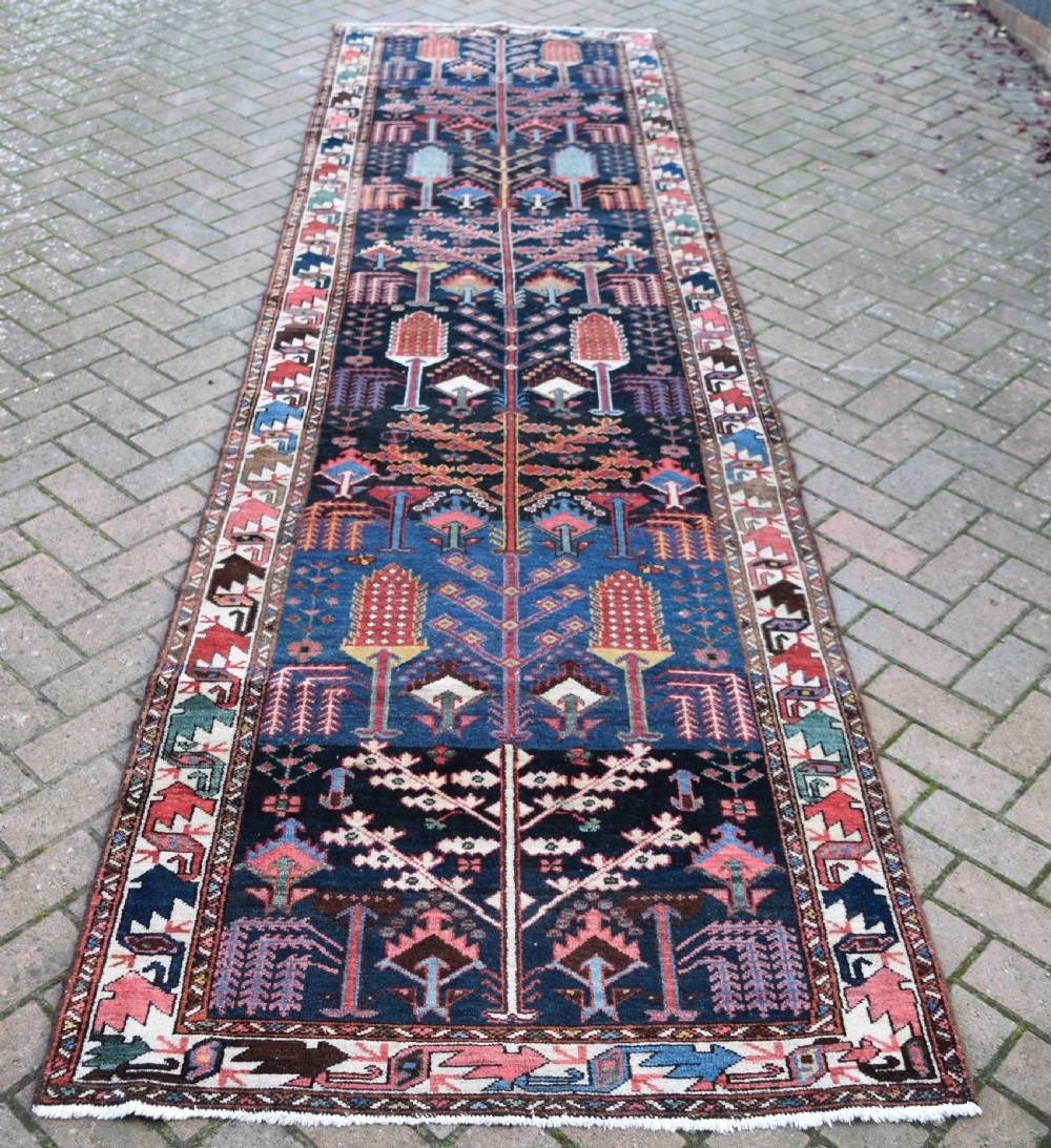 A long antique Persian Bakhtiari runner rug featuring stylised tree motifs in red, blue, and pink on a dark navy ground with a geometric border. View V